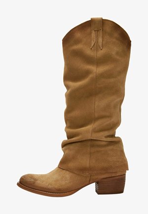 Tan suède kniehoge laarzen met een versleten ontwerp, ronde neus en een gestapelde houten hak. De bovenkant heeft een trekstrip voor gemakkelijke aantrekking.