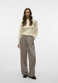 Crème trui met getextureerde mouwen in combinatie met wijde taupe broek. Het schoeisel is zwart met een gladde afwerking. Eenvoudig, neutraal kleurenpalet.