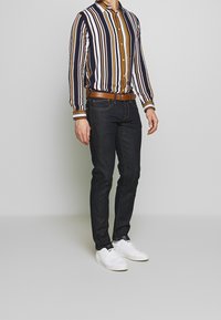 Raidallinen nappipaita laivastonsinisen, valkoisen ja sinappikeltaisen sävyissä, yhdistetty tummiin farkkuihin ja valkoisiin tennareihin. Paita on klassisella kaulusmallella ja siinä on edessä napit.