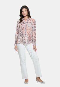 Blusa a maniche lunghe con stampa animale rosa e beige, realizzata in un tessuto morbido, abbinata a pantaloni bianchi a gamba dritta e tacchi argentati.