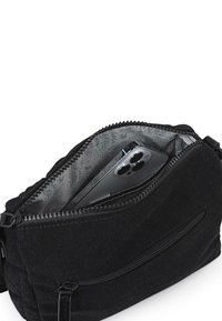 Bolso bandolera de pana negra con abertura con cremallera, que presenta un interior gris con diseño y un smartphone visible en su interior.