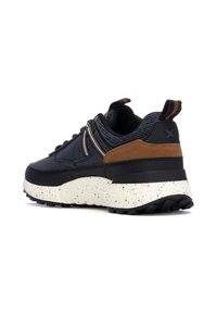 Zapatillas con una parte superior de color azul oscuro, acentos de gamuza marrón, detalles de textil gris y una suela de espuma blanca moteada con un acabado de goma negra texturizada.