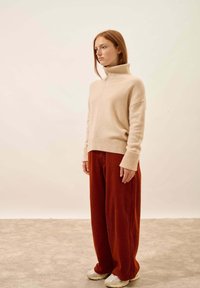 Beżowy sweter kaszmirowy z wysokim ryżowym kołnierzem i bocznymi szczelinami, połączony z szerokimi spodniami z kordurowej tkaniny w kolorze rdzy i kremowymi sneakersami.