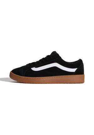Zapatilla negra de caña baja con ralla lateral blanca y suela de goma marrón, vista desde el lateral exterior sobre fondo blanco.