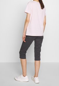 Světle růžové bavlněné tričko a tmavě šedé zkrácené kalhoty. Zobrazené bílé tenisky. Rovný střih, krátké rukávy a minimální detaily.