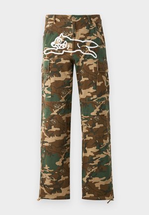 Pantalones cargo en estampado de camuflaje con tonos de verde y marrón, con un gráfico blanco de una criatura saltando en el muslo.
