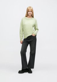 Lysegrønn strikket genser med rund hals, kombinert med mørkegrå vide jeans og svarte platåsko. Enkel design uten mønster.