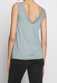 Light blue tank top featuring a V-shaped back and lace trim on the straps. Soft fabric with a smooth texture, paired with dark jeans.