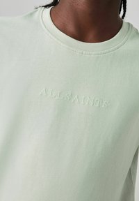 Svetle zelené bavlněné tričko s embosovaným textem "ALLSAINTS" na hrudi, kulatým výstřihem a hladkou texturou.