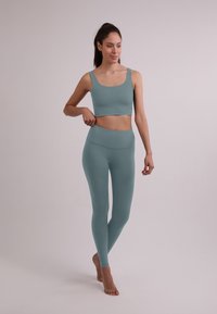 Top corto di un verde teal chiaro e pantaloni a vita alta abbinati, realizzati in tessuto liscio e elastico. Il design presenta spalline larghe e una silhouette aderente.