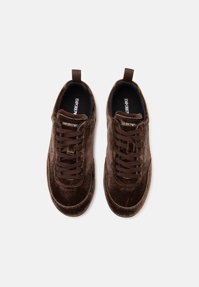 Ζευγάρι σκούρα καφέ βελούδινα sneakers με κορδόνια, θηλιές έλξης και επώνυμες εσωτερικές σόλες σε απλό ανοιχτό φόντο.