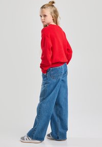 Red, long-sleeve sweater paired with loose-fit, high-waisted blue denim jeans. Gray and white striped shoes complete the outfit.
