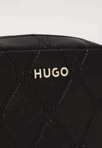 Sac en cuir noir avec un design matelassé et le logo "Hugo" en relief. Les accents dorés et les coutures contrastées créent une texture détaillée.