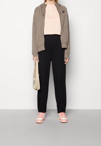 Nike zip-up hoodie i brun, ljusrosa T-shirt, svarta tapered byxor och rosa/vita sneakers. Beige väska med en slät yta.