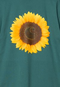 Camiseta de manga corta en un color teal oscuro con un gran gráfico de un girasol amarillo vibrante centrado en la parte delantera, con un centro marrón texturizado.