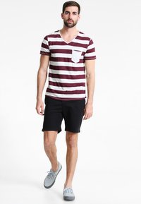 Tricou cu mânecă scurtă, de culoare maroon cu dungi albe, de tip V, cu un buzunar pe față, asociat cu pantaloni scurți negri și adidași gri. Croială casual.