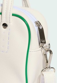 Bílá kožená taška s zelenými akcenty, která má stříbrný zip, nastavitelný popruh a detail s logem. Hladký povrch s šitými detaily.