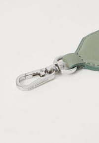 Grønn lærnøkkelring med sølv metallhardware, med klipsfeste og preget merkevare. Glatt tekstur og rene linjer.