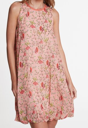 Różowa sukienka bez rękawów z kwiatowym i motylim wzorem, luźnego kroju, noszona przez osobę trzymającą dół sukienki po prawej stronie.