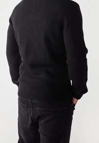 Czarny sweter z dzianiny z prążkowanym dołem, widziany z tyłu, w połączeniu z ciemnymi dżinsami, ukazujący teksturę i dopasowany krój.