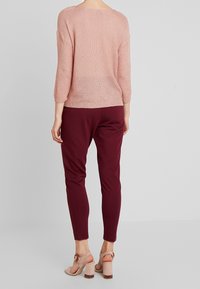 Jasnoróżowy sweter z dzianiny z rękawami trzyczwartowymi, w zestawieniu z burgundowymi spodniami o zwężanym kroju oraz jasnoróżowymi sandałami na blokowym obcasie.