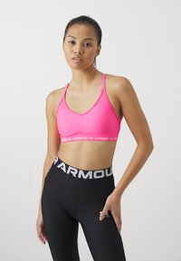 Rožinė sportinė liemenėlė su plonomis petnešėlėmis, turinti V formos iškirpę ir logotipo juostą. Sujungta su juodomis kelnaitėmis aukštu juosmeniu ir logotipo juosta.