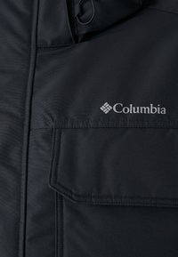 Czarna kurtka Columbia z zapięciem na zamek, teksturowanym materiałem, wyraźnymi klapami oraz logo po prawej stronie.