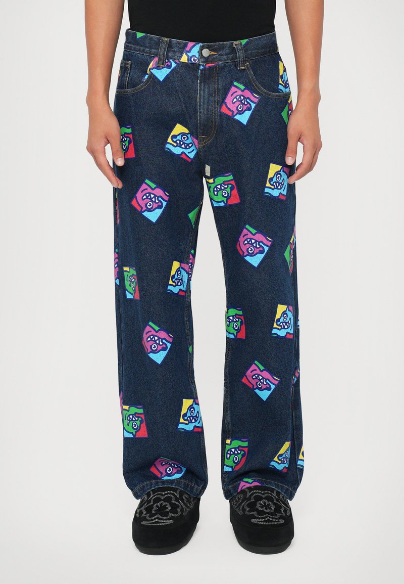 Jeans din denim largi cu o nuanță închisă, decorate cu grafica unor desene animate colorate dispuse în pătrate, incluzând accente de roz, albastru, verde și galben.