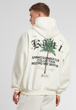 Sweatshirt à capuche crème avec un graphique de palmier, texte en grand imprimé, poignets côtelés et une coupe décontractée. Le tissu semble doux et texturé.