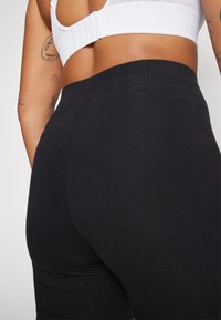 Sorte leggings lavet af strækbart stof, med en høj talje og en glat overflade, vist fra en bagvinkel.