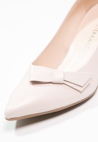 Chaussure plate pointue rose pâle avec un nœud décoratif sur l'avant et une finition en cuir lisse.