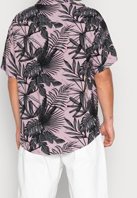 Koszulka z krótkim rękawem w jasnoróżowym kolorze z czarnym wzorem tropikalnych liści. Luźny fason z zaokrąglonym dołem i dyskretnym logo na materiale.
