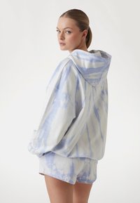 Svijetloplava tie-dye dukserica s labavim krojem i velikom kapuljačom, uparen s odgovarajućim šortsevima. Mekana tkanina s glatkom teksturom i opuštenim dizajnom.