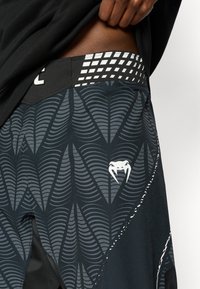 Μαύρα αθλητικά σορτς με γκρι μοτίβο που μοιάζει με κύματα, λευκή αντίθετη λογότυπο και δομημένη μέση με λεπτομέρειες πλέγματος.