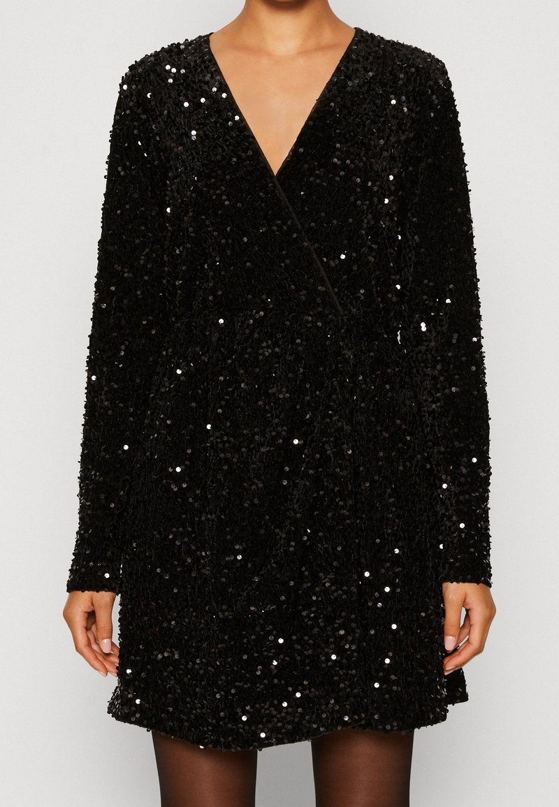 Svart paljettklänning med långa ärmar, V-ringning och en omslagdesign. Har en texturerad yta och en figursydd midja, som sträcker sig till mitten av låret.