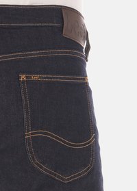 Donkerdenim jeans met een achterzak, oranje stiksels en een leren taillebandlabel in bruin met het woord "Lee" erin geperst.