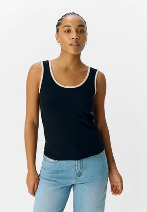Svart ribbad linne med rundad halsringning och crèmefärgad kant. Bärs med ljusblå jeans som har en slät struktur och en åtsittande design.