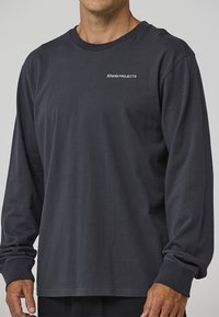 Camiseta de manga larga color gris oscuro hecha de algodón, con cuello redondo y logo bordado en el pecho. Textura suave y ajuste relajado.