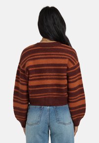 Übergroßer Pullover in Maroon und Rost mit horizontalen Streifen. Gestrickte Textur, gerippter Kragen und Bündchen, kombiniert mit hoch-taillierten blauen Jeans.