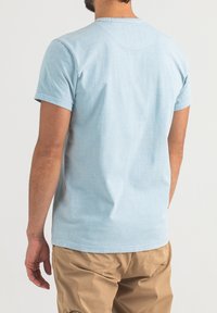 Hellblaues Baumwoll-T-Shirt mit kurzen Ärmeln, Rundhalsausschnitt und lockerer Passform, von hinten gezeigt mit sichtbaren Nähdetails.