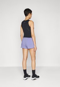 Black athletic tank top with colorful stitching, paired with light purple shorts. Worn with black sneakers and dark socks.
