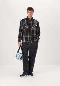 Brown plaid shirt with green and white lines, two chest pockets. Dark gray corduroy pants, blue shoulder bag, and black sneakers.