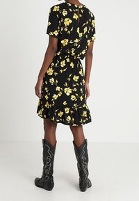 Musta kukkamekko, jossa on keltaisia kukkia, lyhyet hihat, kootut vyötärö ja röyhelöhelma, yhdistettynä mustiin cowboy-kengiin, joissa on koristeellista ompelua.