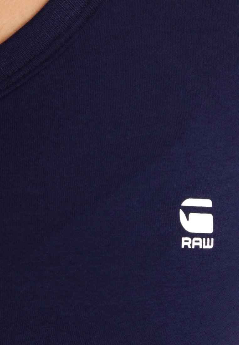 Námořnická modrá tričko vyrobené z měkké bavlny, s kulatým výstřihem a bílým logem "G RAW" na levé straně. Hladká textura.