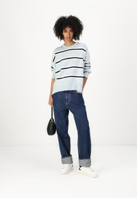 Hellblauer gestreifter Pullover mit schwarz-weißen Streifen, kombiniert mit locker sitzenden dunkelblauen Jeans mit aufgerollten Säumen und weißen Turnschuhen. Kleine schwarze Tasche.