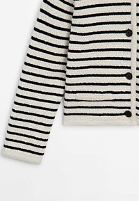 Cardigan tricoté à manches longues avec rayures horizontales crème et noires, poche avant et boutons noirs sur fond blanc.