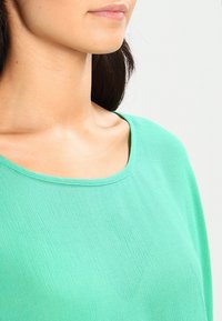 Top verde leggero con scollo rotondo e maniche corte, caratterizzato da una texture liscia e un sottile motivo a costine.