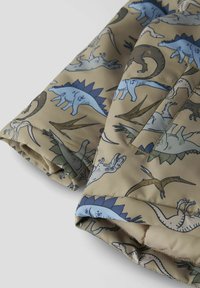 Tissu à motifs de dinosaures en beige avec des illustrations en bleu, vert et noir. Texture lisse avec des coutures visibles et un détail de poche.