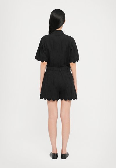 Schwarzer kurzer Anzug mit Puffärmeln, gewelltem Saum, strukturiertem Stoff und taillierter Passform. Entworfen für einen maßgeschneiderten Look mit minimalem Zubehör.