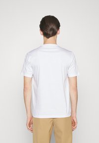 White cotton t-shirt with short sleeves and a crew neckline, featuring a smooth texture and a tag on the left side seam.
